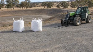 Bulk bags and a parked telehandler beside an empty farm dam, illustrating preparation for buying bentonite.